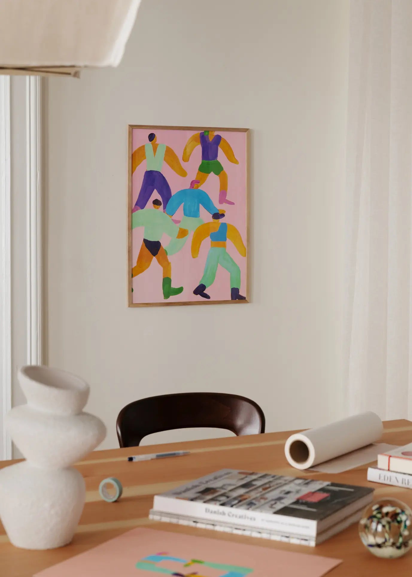 A modern workspace featuring art supplies, books, and decor on a wooden desk. On the beige wall hangs The Poster Club Lise Uhrskov - Walk The Walk (30x40) print, adding a colorful abstract touch to the background.