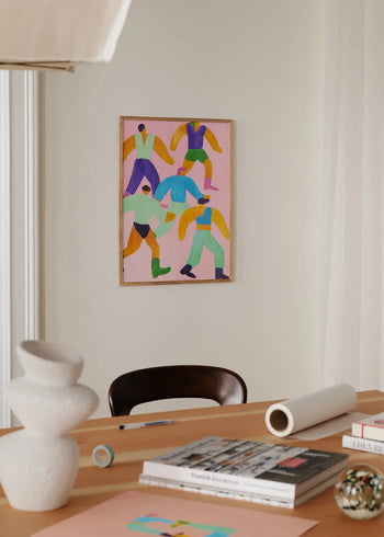 A modern workspace with a wooden desk topped with books, papers, a sculptural vase, and a decorative sphere, featuring The Poster Club Lise Uhrskov - Walk The Walk (50x70) fine art print hanging on the beige wall.
