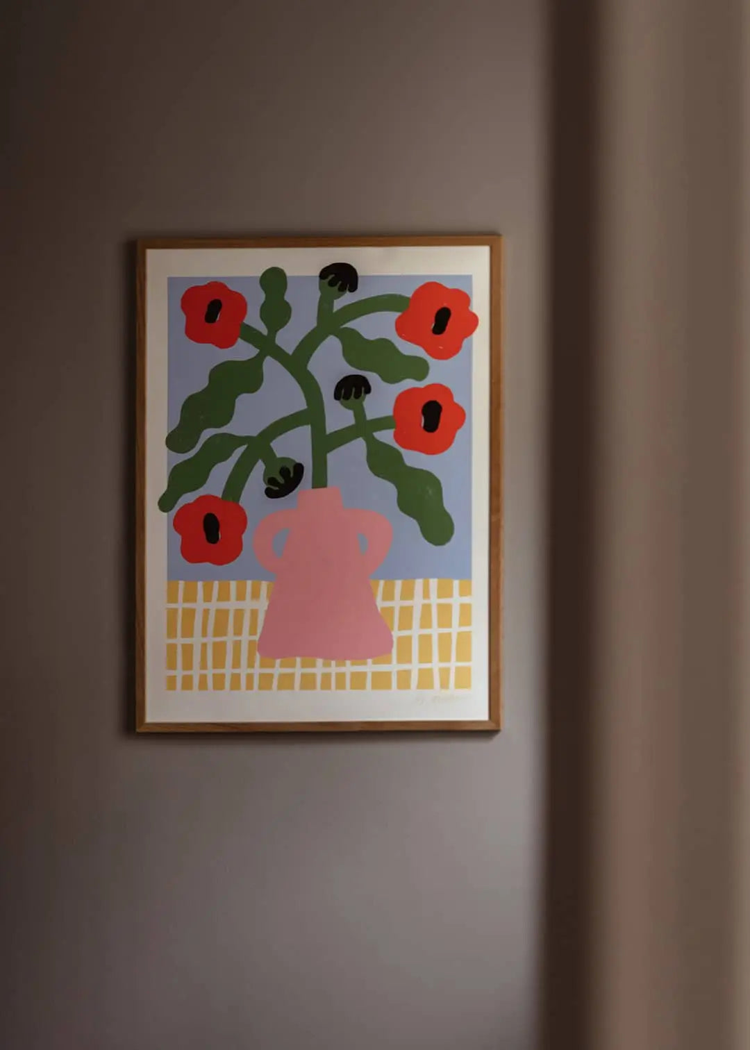 The Poster Club Madelen Möllard - Red Poppies in Pink Vase (50x70) art print features five red flowers in a pink vase with green stems, set on a yellow and white checked tablecloth against a light blue background.
