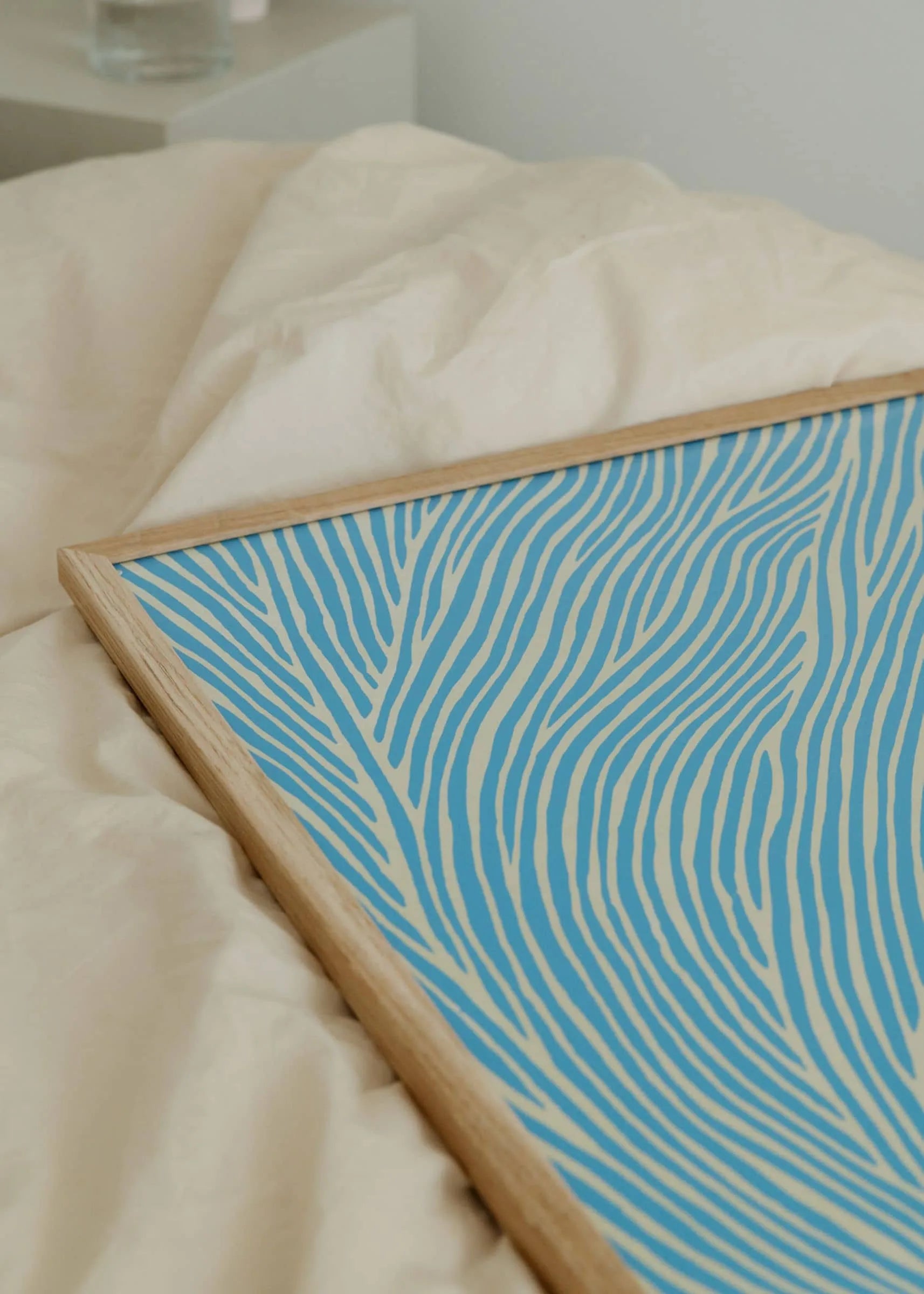 The Poster Club’s Rebecca Hein - The Line - Blue (30x40) art print features blue and cream waves in a refined Nordic design, displayed on a rumpled cream fabric surface.