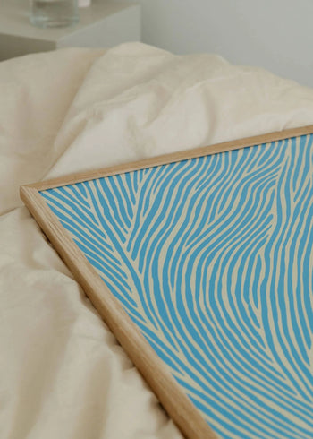 The Poster Club’s Rebecca Hein - The Line - Blue (30x40) art print features blue and cream waves in a refined Nordic design, displayed on a rumpled cream fabric surface.