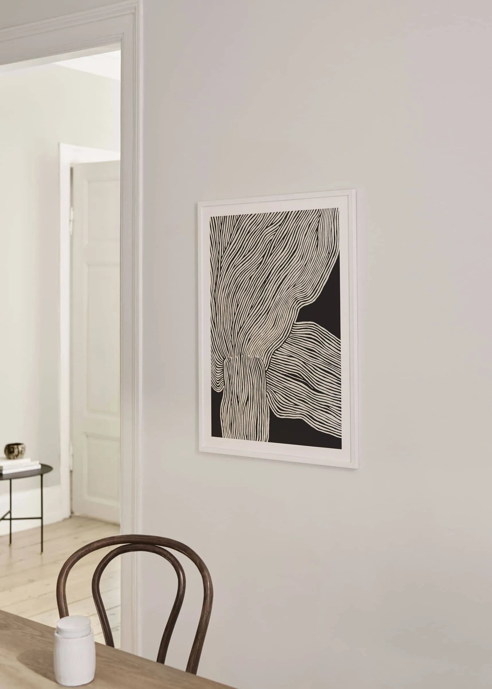 Minimalist interior with a wooden chair, small round table and The Poster Club’s Rebecca Hein - The Line No. 13 (30x40) art print displayed on a light wall, capturing nordic design next to an open doorway.