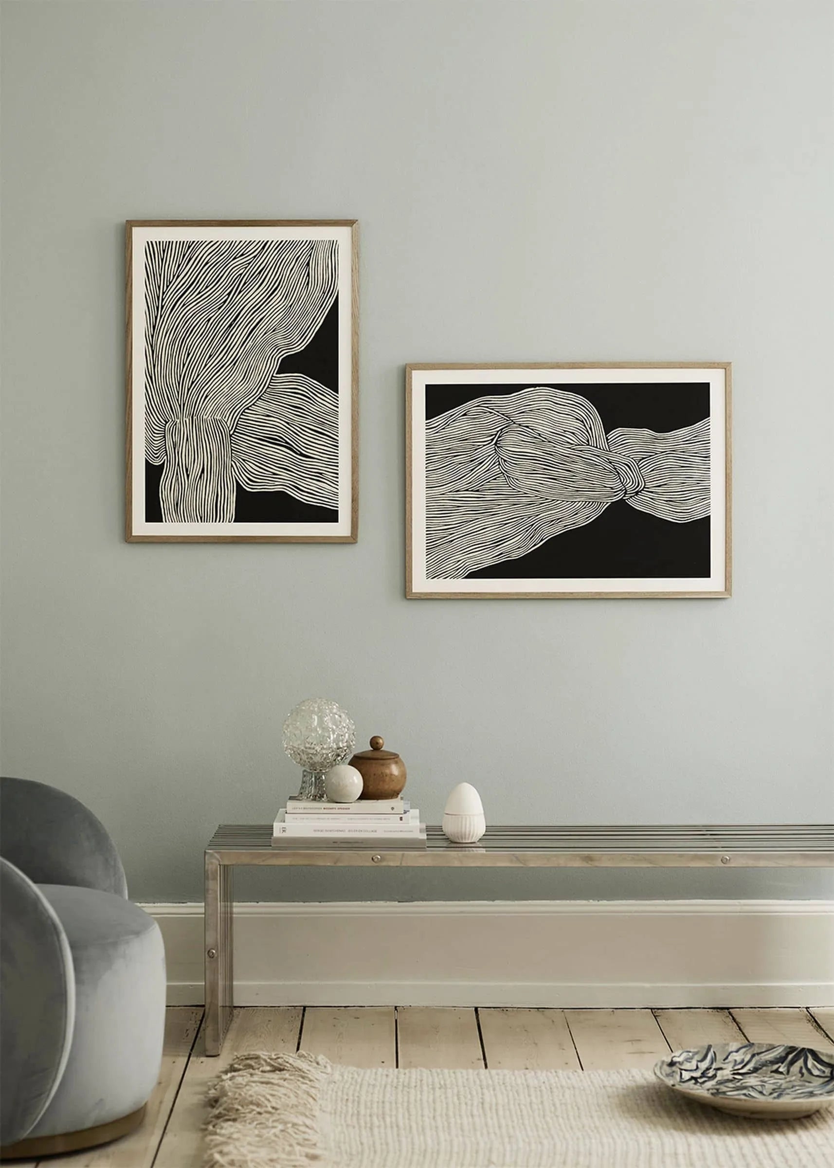 A minimalist room with light walls features The Poster Clubs Rebecca Hein - The Line No. 13 (30x40) print in a wooden frame, capturing Nordic style. A clear acrylic bench displays decor, while a gray chair appears in the corner.