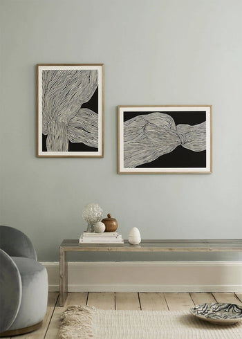 A minimalist room with light walls features The Poster Clubs Rebecca Hein - The Line No. 13 (30x40) print in a wooden frame, capturing Nordic style. A clear acrylic bench displays decor, while a gray chair appears in the corner.