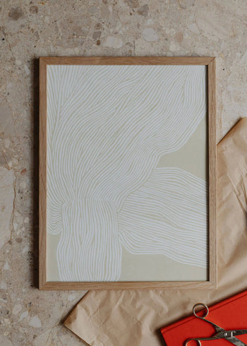 The Poster Clubs Rebecca Hein - The Line No. 9 (30x40) framed art print showcases white wavy lines on beige, styled on a speckled stone surface with brown wrapping paper, an orange notebook, and metal scissors.
