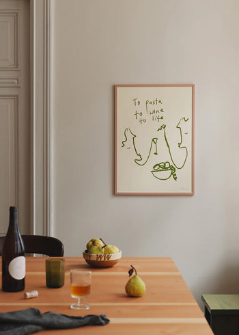 A cozy dining table with pears, wine, glasses, and fruit sits below The Poster Club Ruby Hughes - To Life (50x70) giclée print, featuring green “To pasta, to wine, to life” above minimalist sketches.