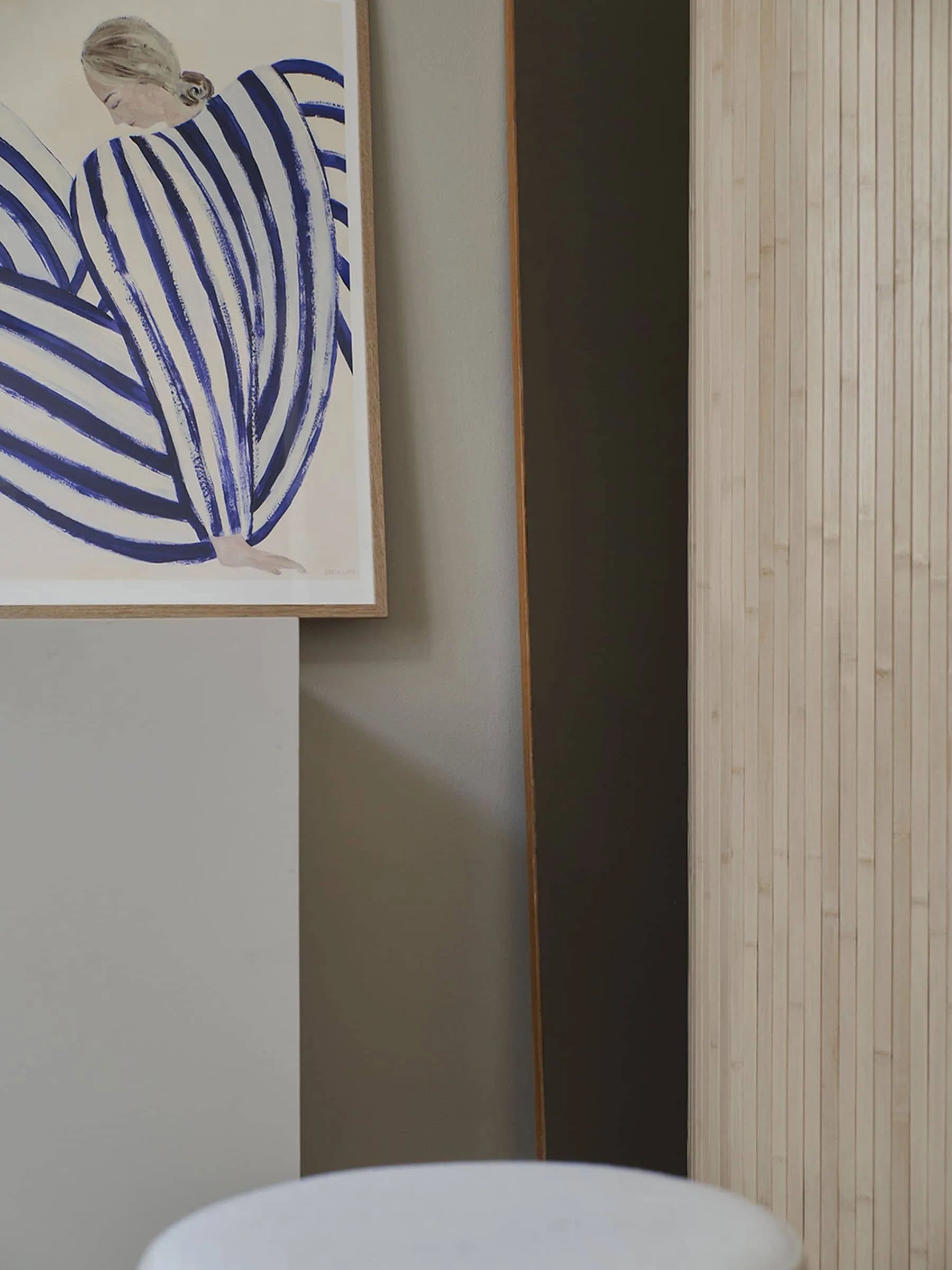 The Poster Clubs Sofia Lind - Blue Stripe At Concorde (30x40) giclée print from the Paris Metro Collection shows a bun-haired figure in blue and white stripes, framed on a neutral wall with light wood paneling and a round white object below.