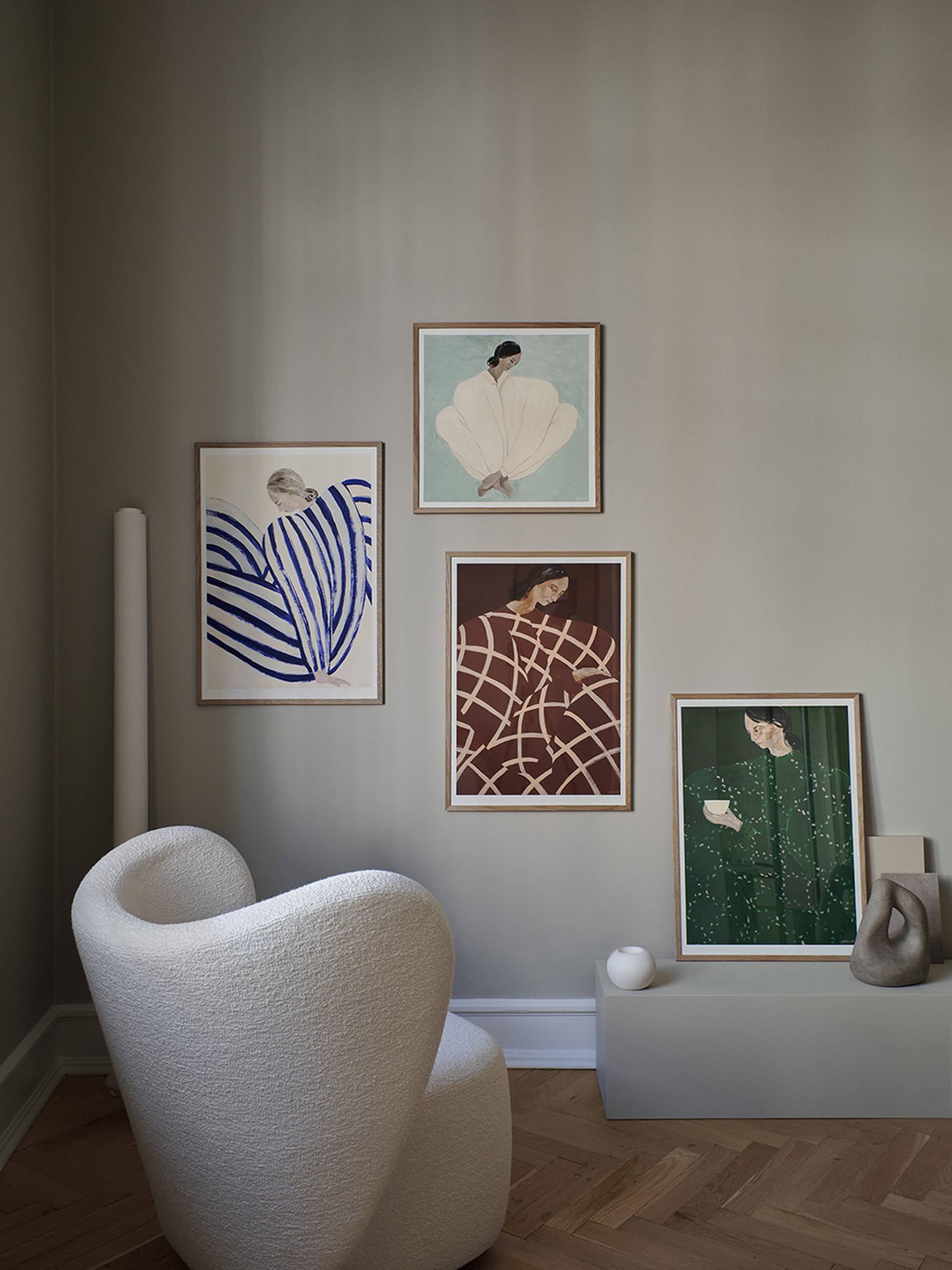 A cozy corner with a white textured armchair, abstract ceramic decor, and The Poster Club Sofia Lind - Blue Stripe At Concorde (50x70) giclée print on a neutral wall above light wood herringbone flooring.