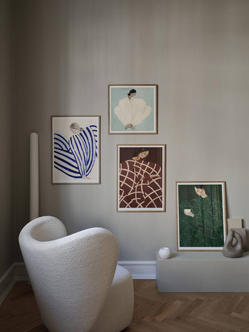 A cozy corner with a white textured armchair, abstract ceramic decor, and The Poster Club Sofia Lind - Blue Stripe At Concorde (50x70) giclée print on a neutral wall above light wood herringbone flooring.