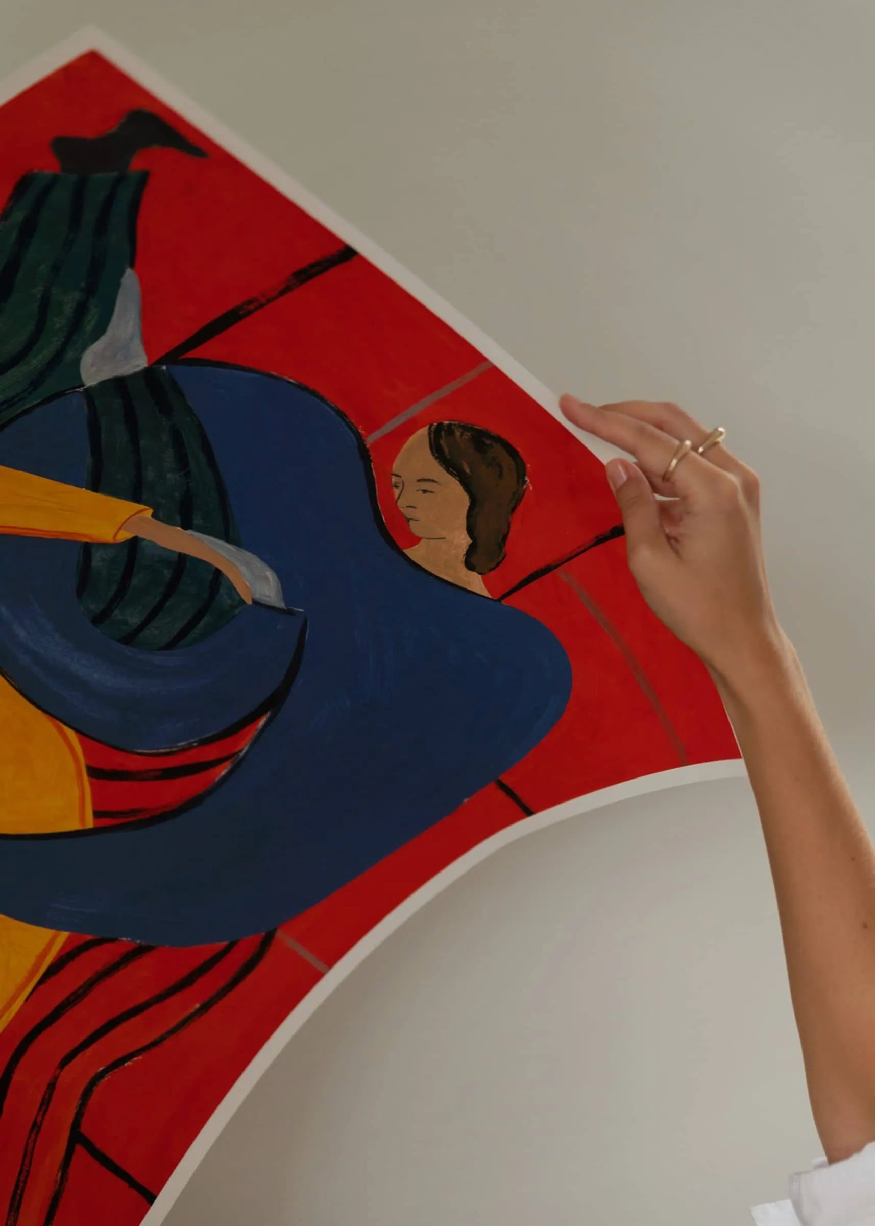 A hand with rings holds up Sofia Lind - Hold You - Red (30x40) from The Poster Club, a vibrant abstract art print of a brown-haired woman set against a red background with blue, green, and yellow shapes.
