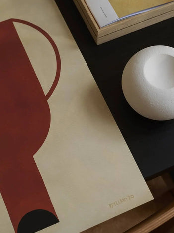 The Poster Club Studio Paradissi - Dialogues 03 (50x70): Minimalist abstract art print with red and black geometric shapes on beige, placed on a dark table with a round white textured object and a closed book. Printed on premium art paper. Brand: The Poster Club.