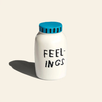A white bottle with a blue cap labeled “FEELINGS” is the Third Drawer Down Adam JK - Feelings Stress Toy by Third Drawer Down, shown on a plain light background with its shadow cast to the left.