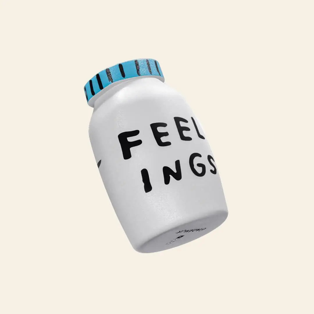 The Third Drawer Down Adam JK - Feelings Stress Toy, a white jar with a blue lid and partially cropped FEELINGS text, rests tilted on a light beige background, echoing the gentle release of emotions.