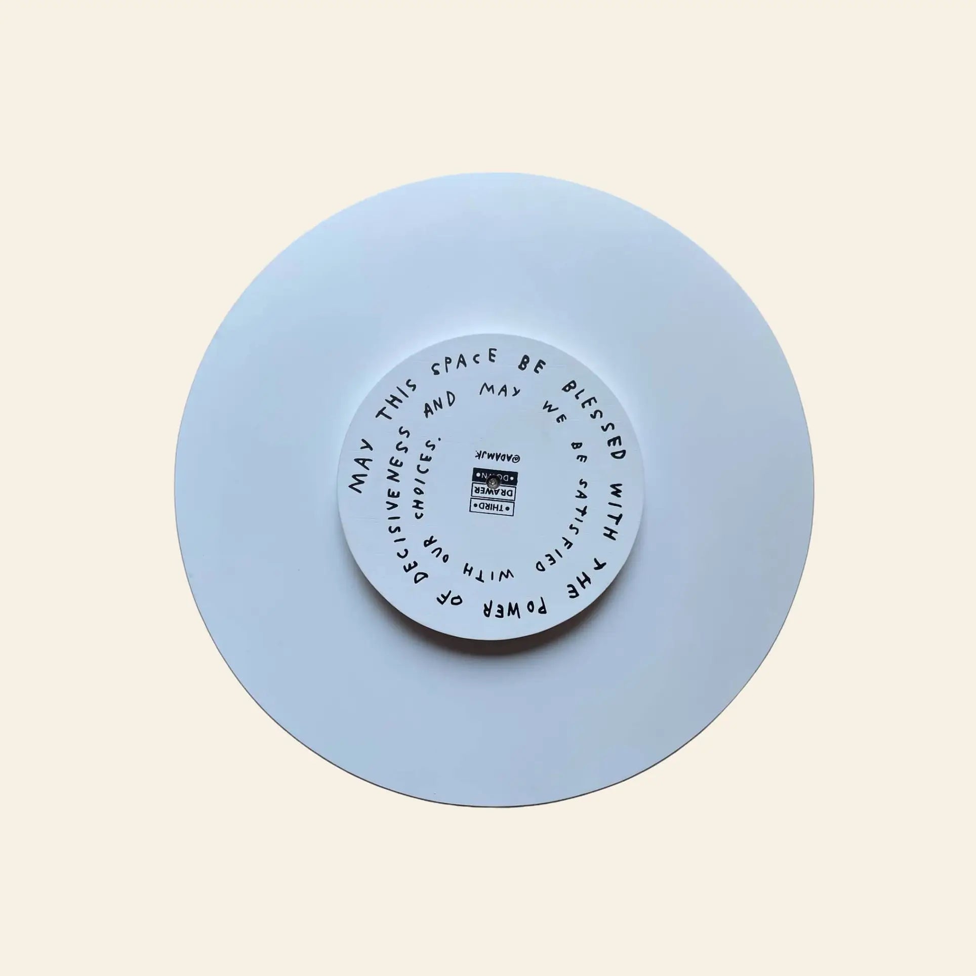 The Third Drawer Down Adam JK - Indecisive Lazy Susan is a white circular piece featuring a smaller inner circle and black handwritten text by Adam JK: May this space be blessed with decisiveness; may we be critical and honest.