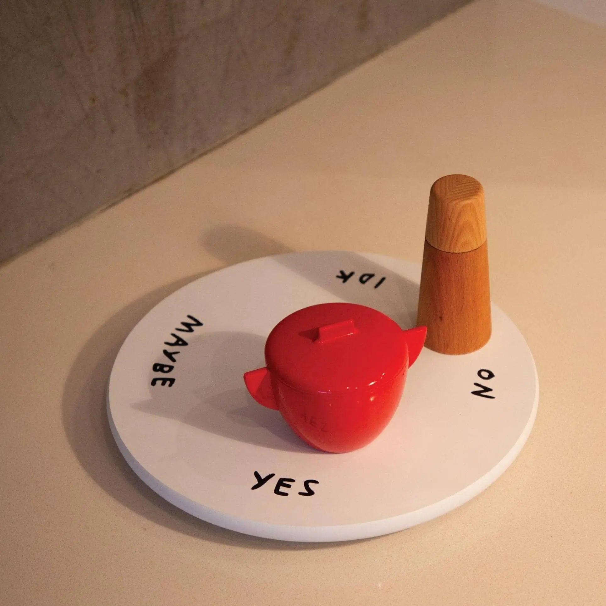 The Third Drawer Down Adam JK - Indecisive Lazy Susan is a playful round white board with YES, NO, MAYBE, and IDK at the edges, plus a red container and wooden spinner—perfect for making decisions fun.