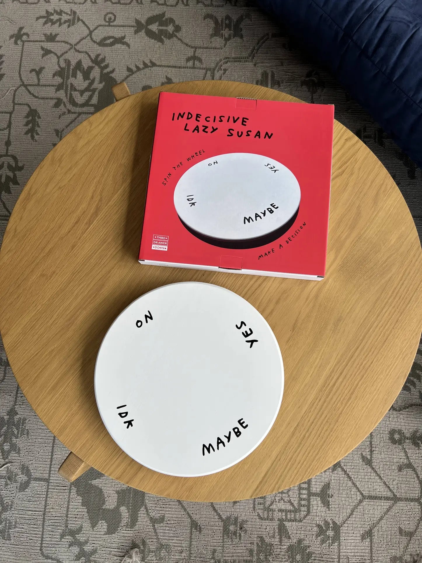 The Third Drawer Down Adam JK - Indecisive Lazy Susan features a round white plate labeled YES, NO, MAYBE, IDK, and ON next to its red box with a matching image—Third Drawer Down’s playful solution for choice-making.