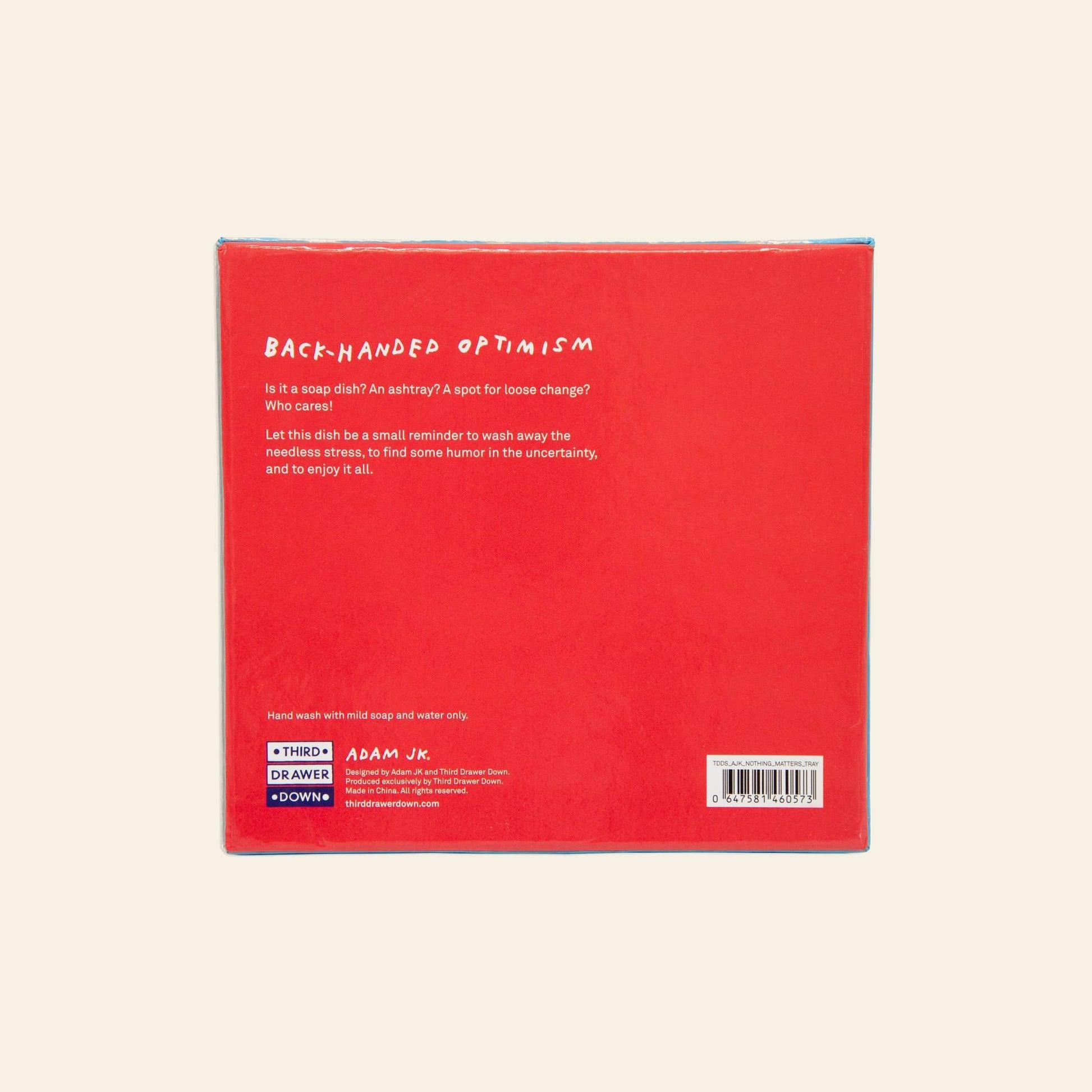 The back of the Third Drawer Down Adam JK - Nothing Matters Ceramic Trays red box features white text describing its playful reminder to find humor in uncertainty. Brand logos and care instructions are shown at the bottom.