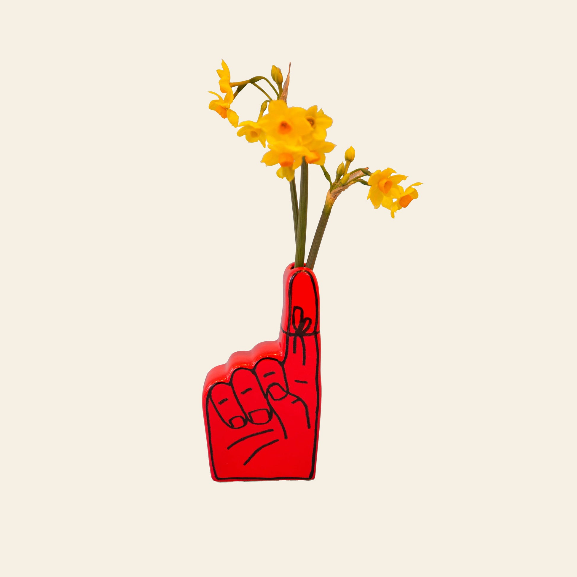 The Third Drawer Down Adam JK - Remember Bud Ceramic Vase, shaped like an upright hand with the index finger raised and holding yellow flowers, is displayed against a plain beige background.