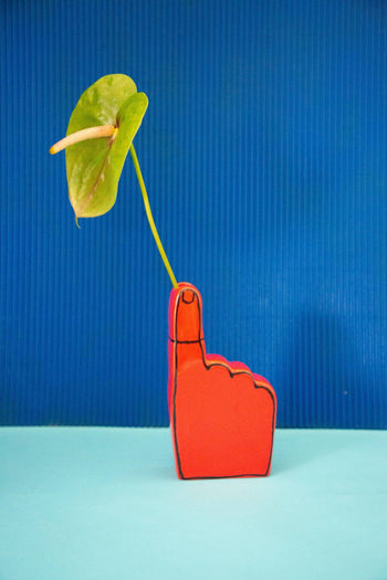 The Third Drawer Down Adam JK Remember Bud Ceramic Vase, shaped like an upward-pointing hand, holds a green anthurium against a blue background—a vibrant tribute to cherished memories.