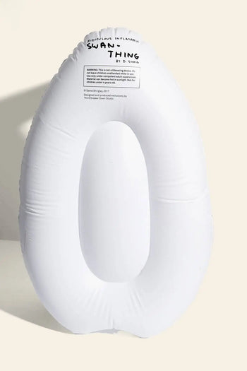 A white, oval inflatable pool float from Third Drawer Down stands upright against a beige background. Black text at the top reads “SWAN THING”—a playful reference to the Third Drawer Down David Shrigley Ridiculous Inflatable Swan-Thing.