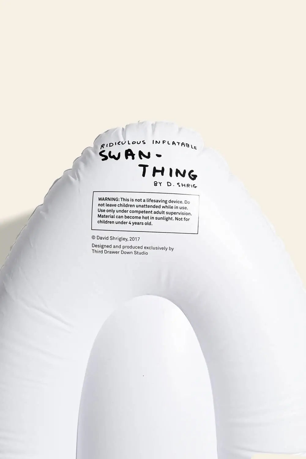 The Third Drawer Down David Shrigley - Ridiculous Inflatable Swan-Thing is a white inflatable swan float featuring printed text by David Shrigley at the top, plus a warning label and extra info on the float.
