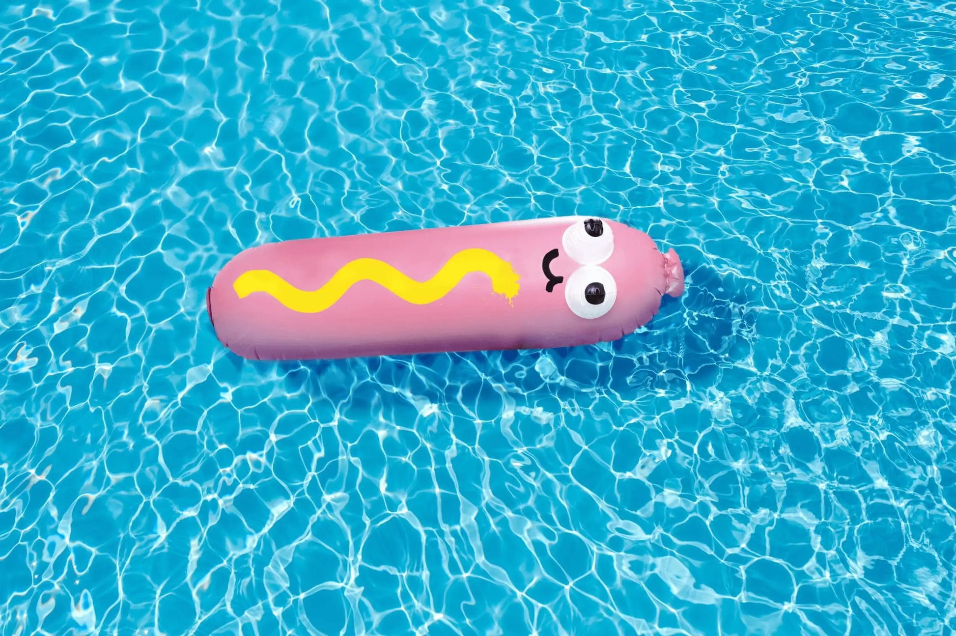 The Third Drawer Down Jon Burgerman - Hot Diggity Dog Pool Float, by Third Drawer Down, features a pink hot dog shape with cartoon eyes, a smile, and wavy yellow mustard—perfect for summer pool parties and fun on the water.