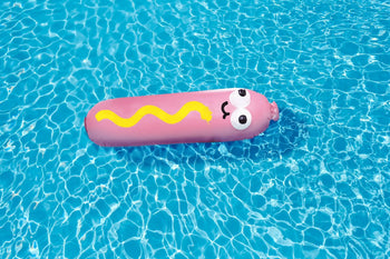 The Third Drawer Down Jon Burgerman - Hot Diggity Dog Pool Float, by Third Drawer Down, features a pink hot dog shape with cartoon eyes, a smile, and wavy yellow mustard—perfect for summer pool parties and fun on the water.