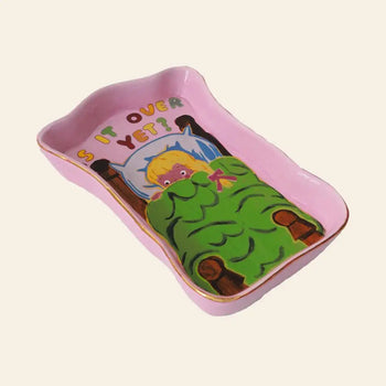 The Third Drawer Down Magda Archer - Is It Over Yet Trinket Tray features a pink ceramic design with an anxious figure hiding under a green blanket and the colorful phrase IS IT OVER YET?—perfect for holding small jewelry.