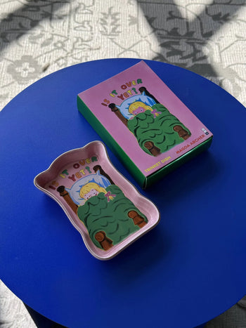 The Third Drawer Down Magda Archer Is It Over Yet? Trinket Tray, featuring a child in bed with a green blanket, sits on a round blue table—a perfect spot for keeping small jewelry.