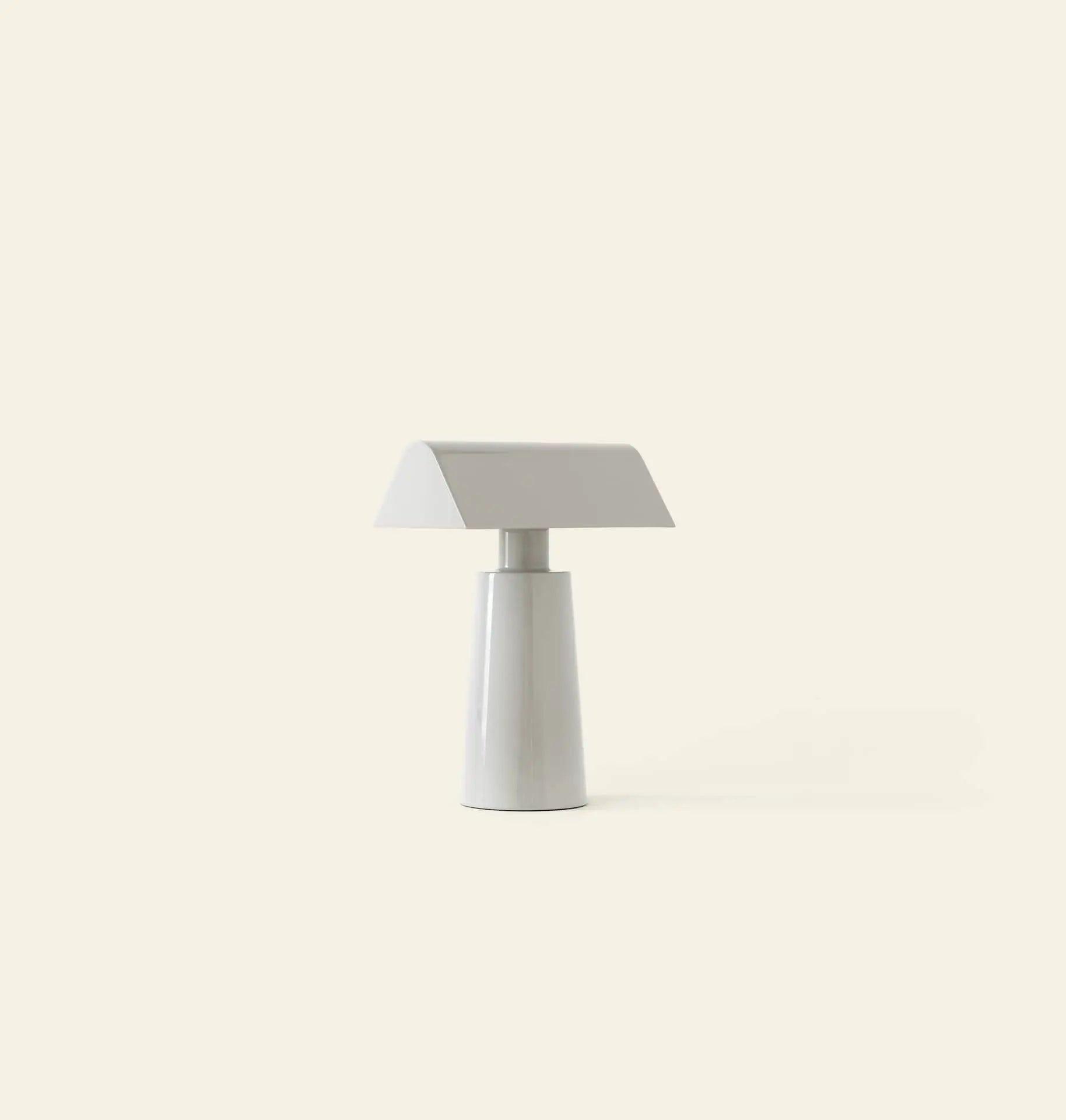 The &Tradition Caret MF1 Portable Table Lamp by &Tradition features a modern, minimalist design with a conical base and flat rectangular shade, bringing sleek style to any space against a plain light beige background.