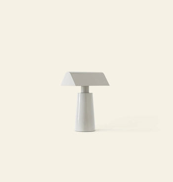 The &Tradition Caret MF1 Portable Table Lamp by &Tradition features a modern, minimalist design with a conical base and flat rectangular shade, bringing sleek style to any space against a plain light beige background.