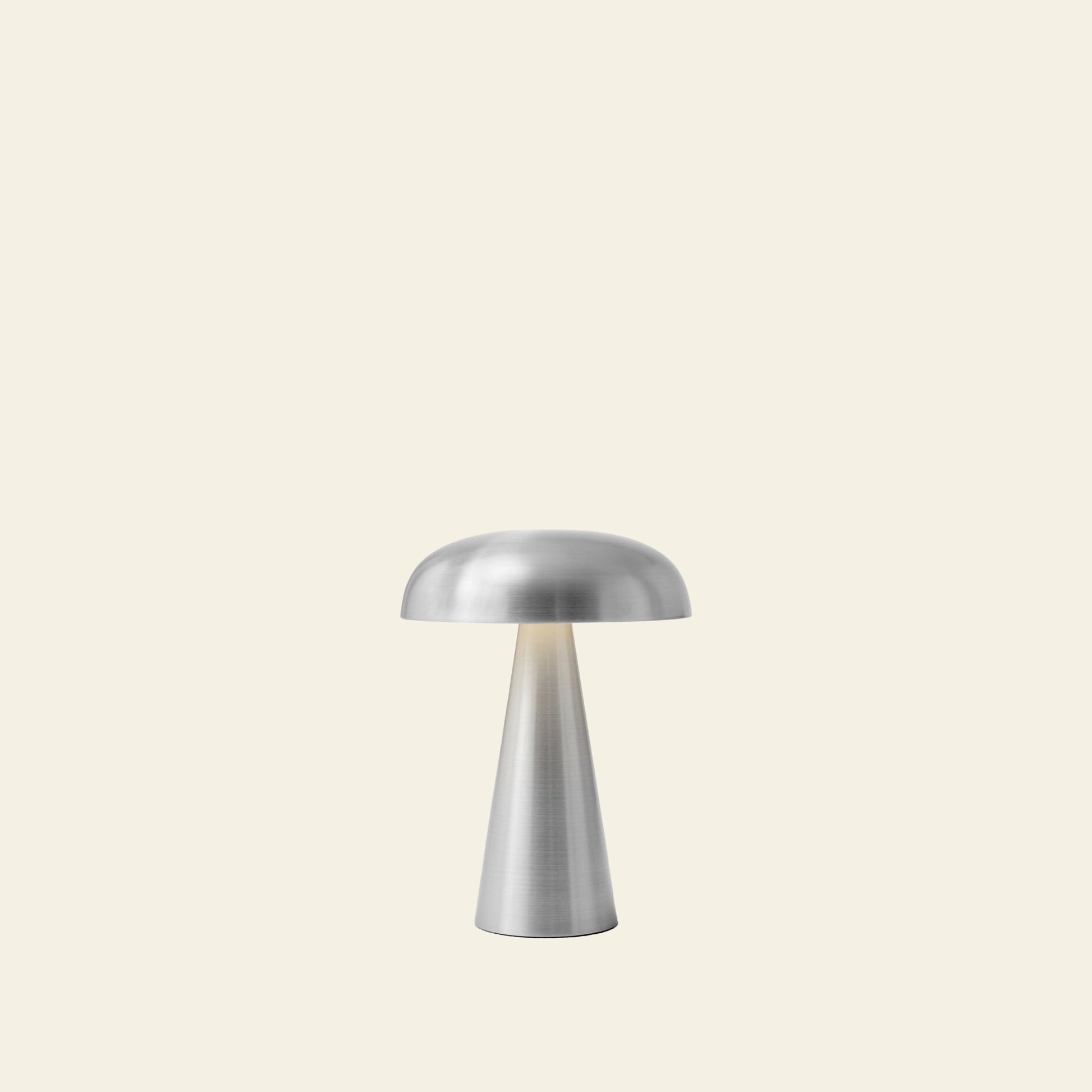 The &Tradition Como SC53 Portable Table Lamp by &Tradition features a modern rechargeable design with a mushroom-shaped shade and conical base, shown here against a plain, light beige background.