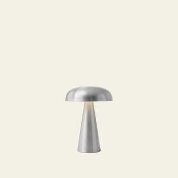 The &Tradition Como SC53 Portable Table Lamp by &Tradition features a modern rechargeable design with a mushroom-shaped shade and conical base, shown here against a plain, light beige background.