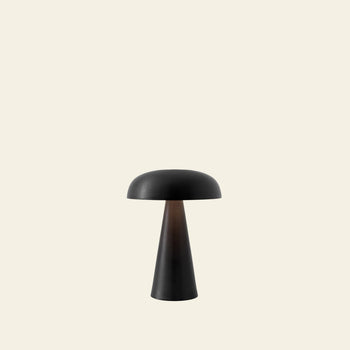 The &Tradition Como SC53 Portable Table Lamp, by &Tradition, features a modern black finish with a dome shade and conical base. Centered on a light beige background, this rechargeable lamp offers adjustable lighting for versatile use.