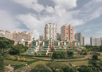 UNIT. A Glimpse Into Singapore’s 1970s - ’80s Private Apartments showcases colorful mid-rise homes set amid greenery and roads, with taller towers in the background beneath a partly cloudy sky.