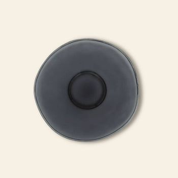 A top view of the Urban Nature Culture Breakfast Plate, crafted from recycled glass with an organic round shape in dark gray, sits on a beige background—ideal for those who cherish sustainable living.