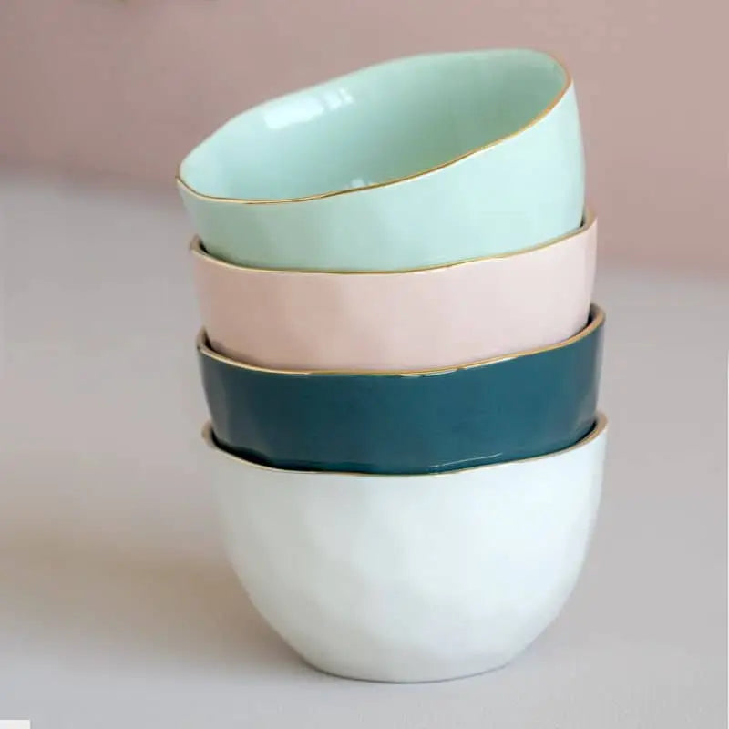 Four Urban Nature Culture Good Morning Bowls in pastel hues—mint green, teal, white, and soft pink—are stacked on a light surface. Each bowl features a thin gold rim and the brand’s signature irregular shape, perfect for your morning meal.