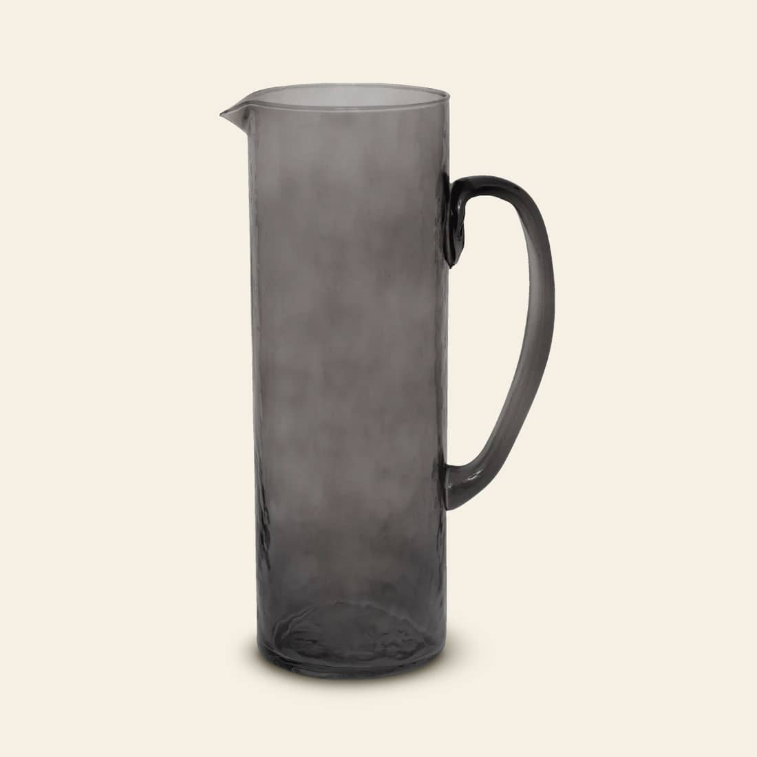 The Urban Nature Culture Jug Recycled Glass is a tall, cylindrical vessel with handle and small spout, featuring translucent gray glass and an elegant silhouette—perfect for adding modern charm to any light space.