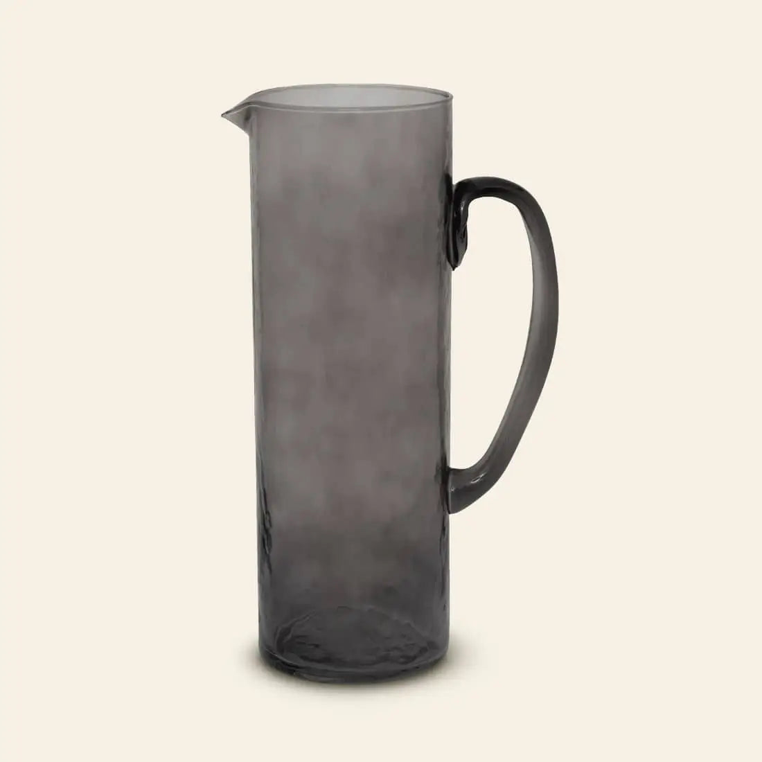 The Urban Nature Culture Jug Recycled Glass features a tall silhouette in translucent gray, with a curved handle and small pouring spout, set against a plain beige background.