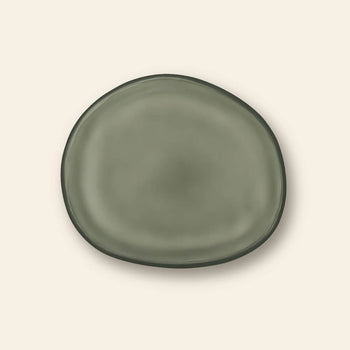 The Urban Nature Culture Plate Recycled Glass Frost, a round plate with uneven edges in earthy olive green tones, is displayed on a light beige background.