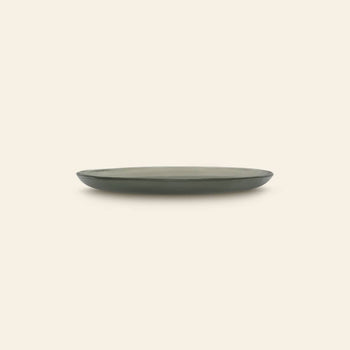 The Urban Nature Culture Plate Recycled Glass Frost is a simple, round recycled plate with a slightly raised rim in dark green, shown from the side against a light beige background.