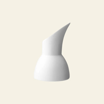 The Vipp Vipp205 Milk Jug by Vipp is a minimalist white ceramic jug with a wide base and distinctive tilted spout, showcased against a plain beige background.