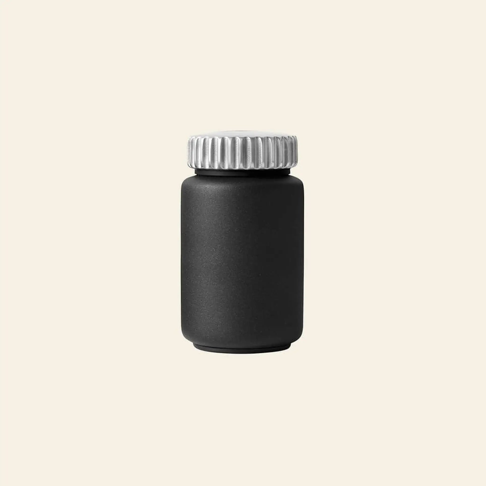 The Vipp263 Salt & Pepper Mill by Vipp stands upright with a matte black bottle and metallic silver screw cap—an ideal addition to your kitchen or for pairing with other Vipp mills featuring a ceramic grinder.