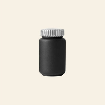 The Vipp263 Salt & Pepper Mill by Vipp stands upright with a matte black bottle and metallic silver screw cap—an ideal addition to your kitchen or for pairing with other Vipp mills featuring a ceramic grinder.