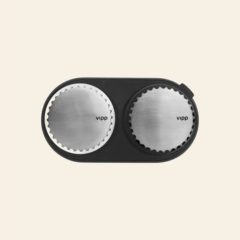 A top-down view of Vipp Vipp263 Salt & Pepper Mills with stainless steel tops and ceramic grinders, elegantly arranged in a black oval tray on a light beige background—an ideal addition to any modern kitchen.