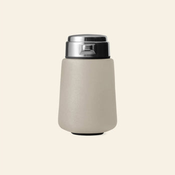 The Vipp Vipp9 Dispenser by Vipp, featuring a modern matte beige finish and silver metallic lid, stands upright against an off-white background—its sleek minimalist design echoes the iconic Vipp aesthetic.