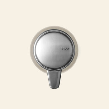 The Vipp Vipp9 Dispenser, featuring a modern stainless steel design and the Vipp logo on the front, is shown mounted on a plain beige background—an elegant and practical kitchen accessory.