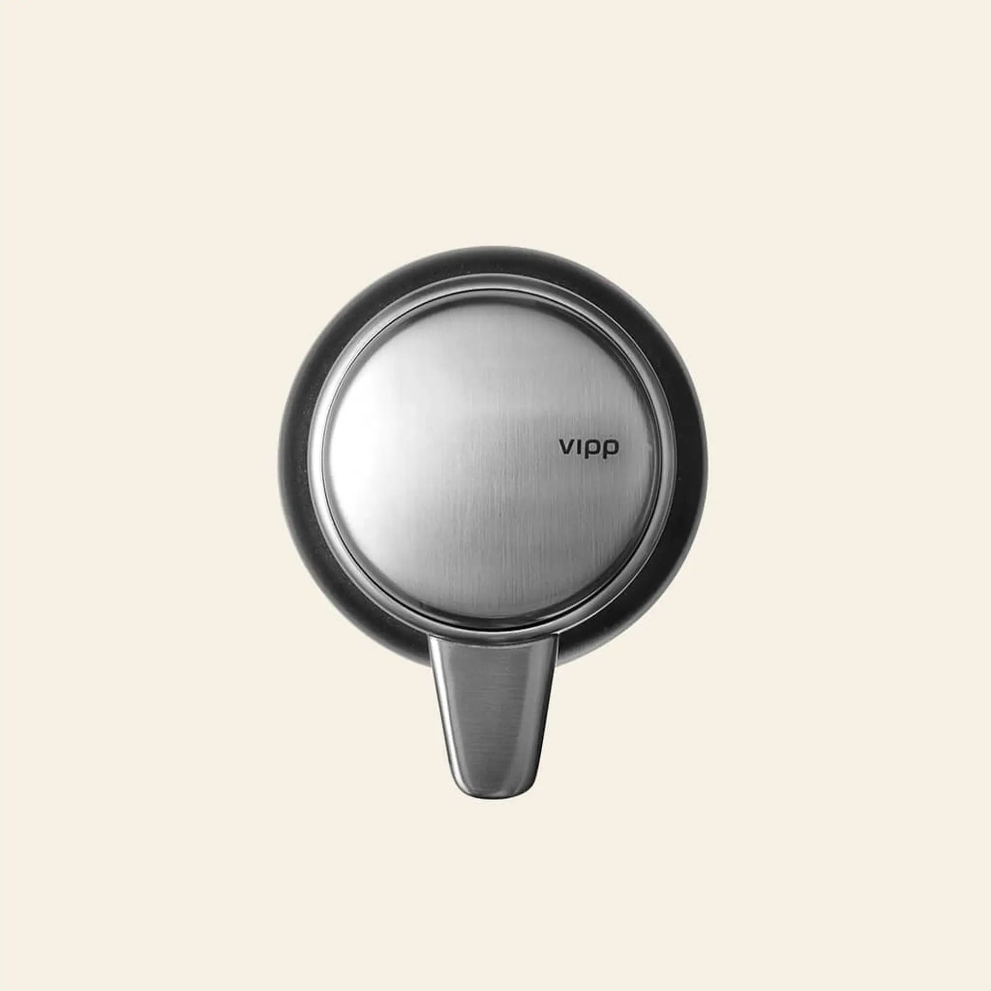 A round, brushed stainless steel wall hook by Vipp is mounted on a beige background—an elegant kitchen detail that pairs seamlessly with the Vipp Vipp9 Dispenser.