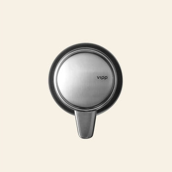 A round, brushed stainless steel wall hook by Vipp is mounted on a beige background—an elegant kitchen detail that pairs seamlessly with the Vipp Vipp9 Dispenser.
