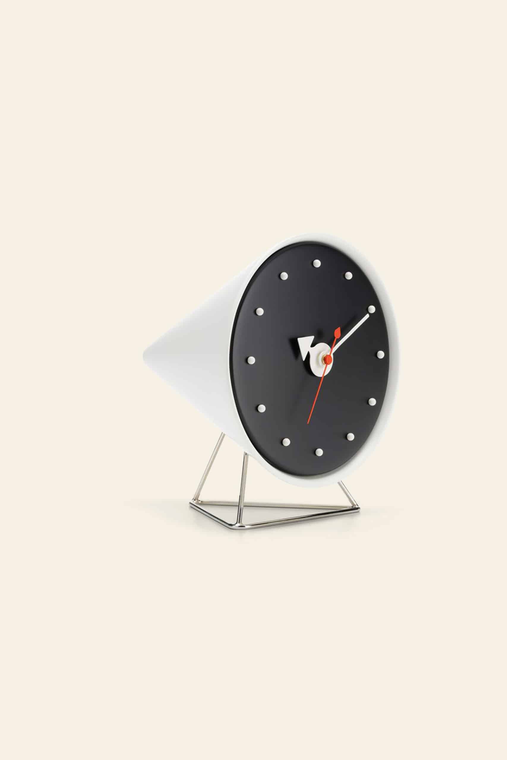 The Vitra Cone Clock by Vitra is a modern, cone-shaped desk clock inspired by the George Nelson design, featuring a black face with white hour markers and hands, a red second hand, and a minimalist metal stand against a light beige background.